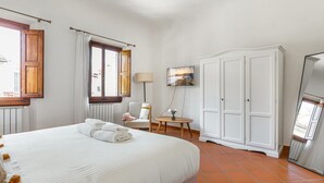 A hotel room with a bed, a chair, a TV, and a wardrobe. - GuestHost - Charming 75 sqm apartment, able to accommodate up to 4 people, located on the FOURTH floor of an ancient building (NO lift). The property is located in the historic center of Florence (Restricted Traffic Area), in the lively Sant'Ambrogio dis (Firenze)