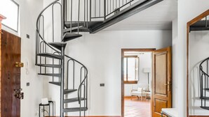 A spiral staircase in a room with white walls, a wooden door, and a tiled floor. - GuestHost - Charming 75 sqm apartment, able to accommodate up to 4 people, located on the FOURTH floor of an ancient building (NO lift). The property is located in the historic center of Florence (Restricted Traffic Area), in the lively Sant'Ambrogio dis (Firenze)