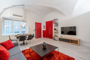 A modern living room with a dining area, a sofa, a coffee table, a TV, and a bookshelf.