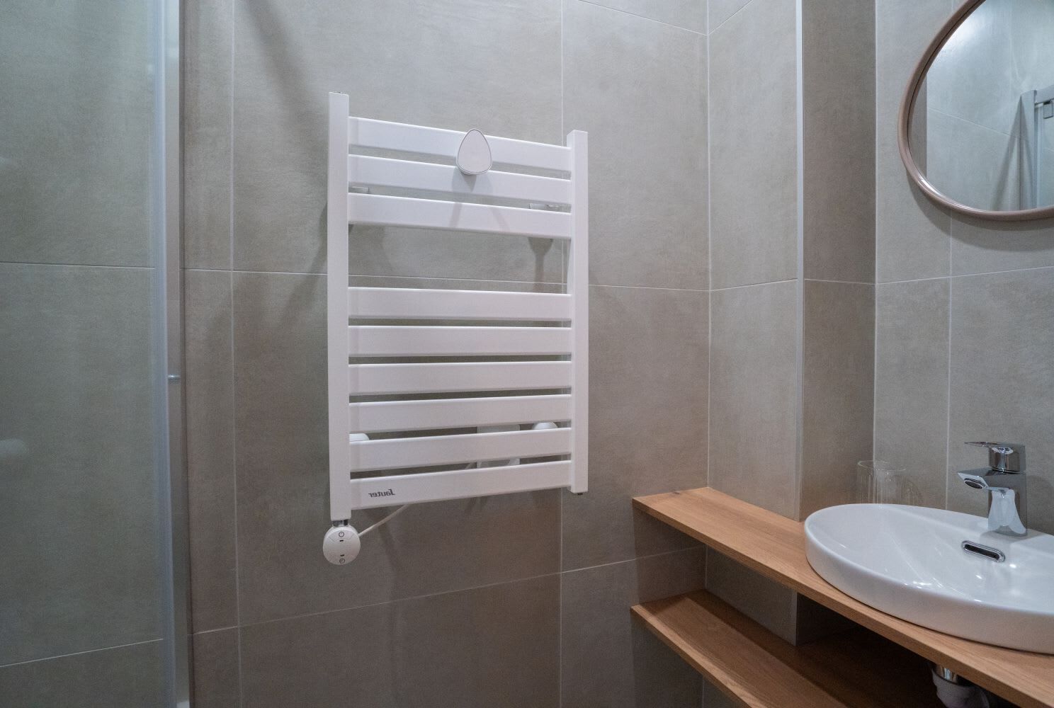 Un baño con toallero blanco, espejo redondo y repisa de madera.