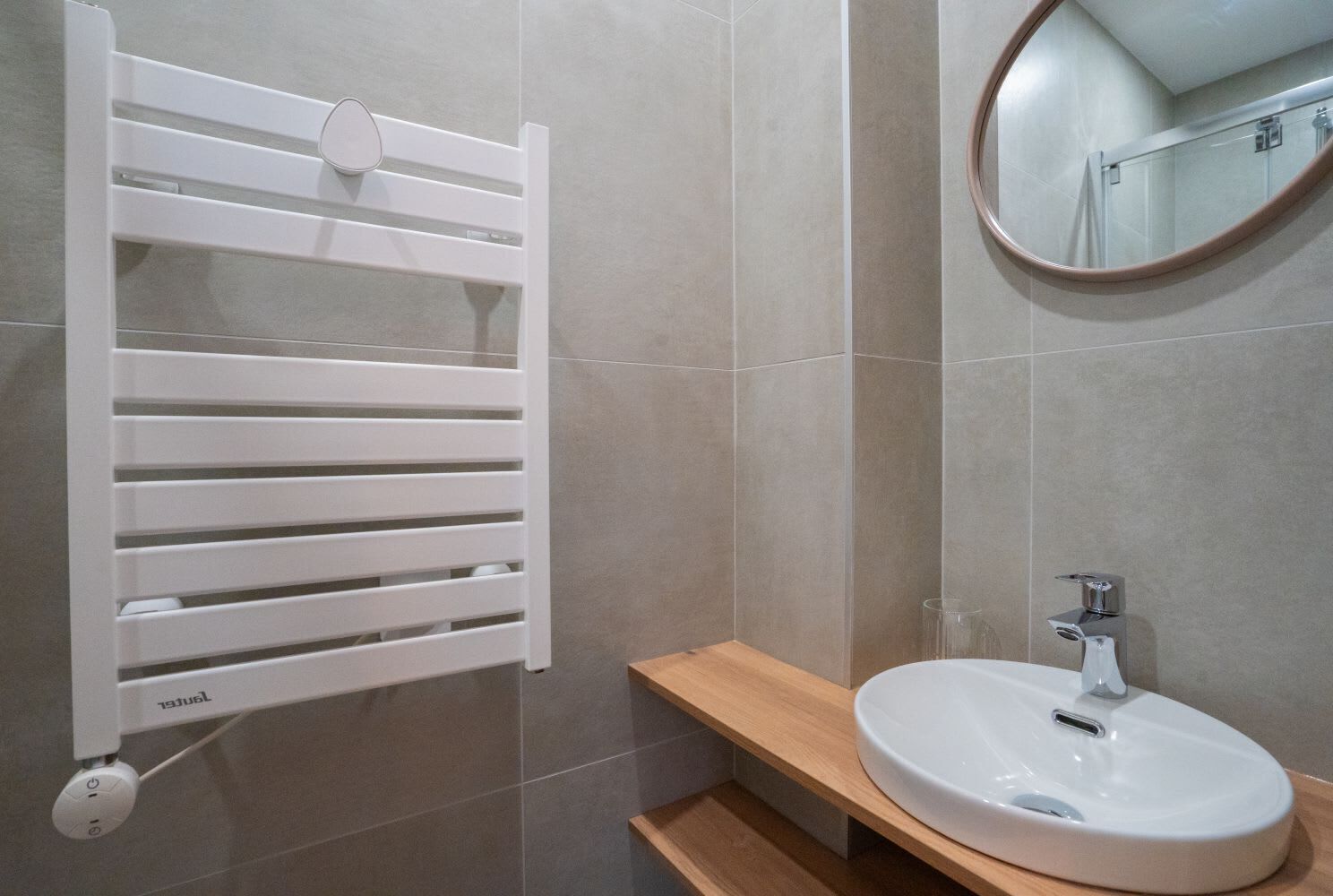 Un baño con toallero blanco, repisa de madera y espejo redondo.