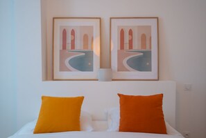 A hotel room with a bed, two orange pillows, and two framed artworks above the bed. - Studio neuf Paris 3ème Métro Etienne Marcel (Paris)