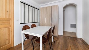 Un coin repas avec une table blanche, des chaises marron, des meubles en bois et une fenêtre avec des stores.