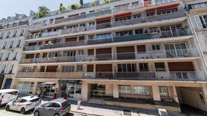 Un immeuble à plusieurs étages doté de balcons, d’un commerce au rez-de-chaussée et de voitures garées.