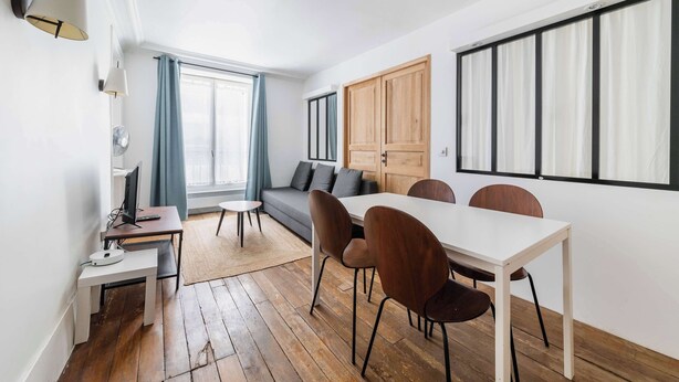 Un salon moderne comprenant un canapé, une table à manger, des chaises, un téléviseur et un meuble en bois.
