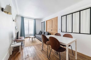 A modern living room with a sofa, dining table, chairs, a TV, and a wooden cabinet. - Appartement Paris 6ème Proche Métro Confortable (Paris)