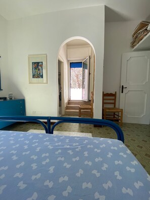 A bedroom with a bed, a desk, a chair, a door, and a staircase leading to a balcony.