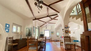 A spacious room with a high ceiling, wooden beams, a dining area with chairs and a table, and a view of the outside through a window. - Splendid detached villa, near the sea (Santa Lucia)