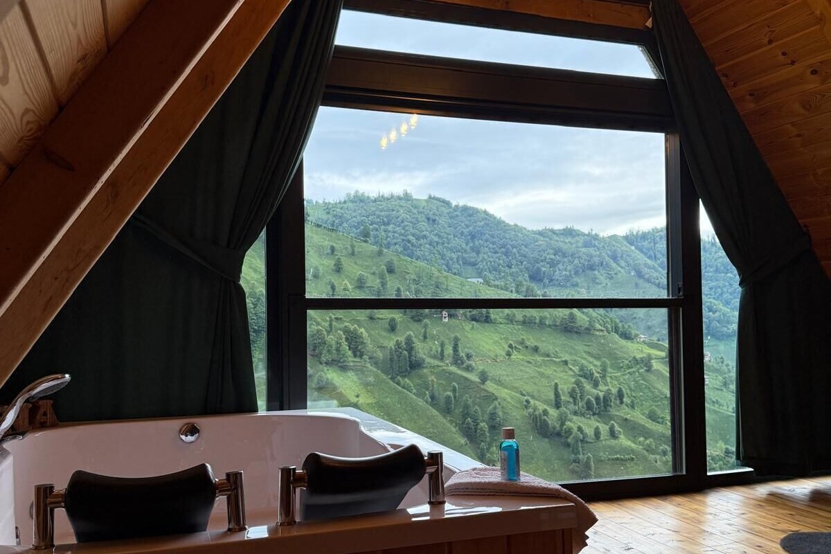 Una cabaña de madera con un ventanal grande que ofrece vistas a colinas verdes.