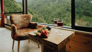 A room with a large window, a wooden table, a patterned armchair, and two wine glasses. - Ena Bungalov (Çamlihemsin)