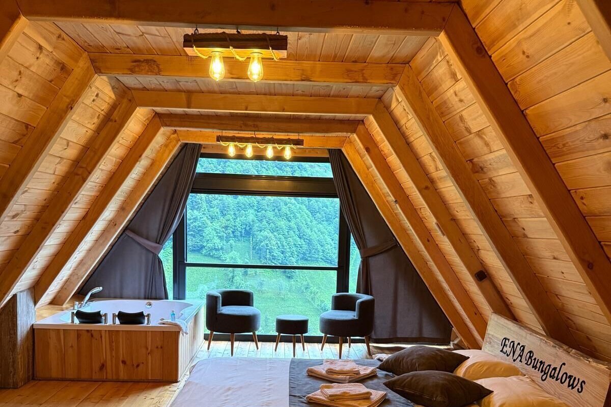 Un dormitorio acogedor en el ático con una cama grande, un escritorio y sillas, que ofrece una vista panorámica del bosque.