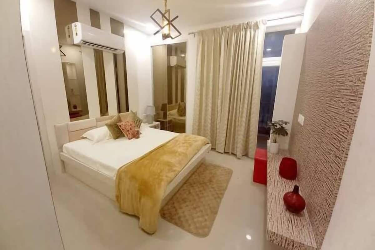 A modern bedroom with a large bed, a bedside table, a mirror, a ceiling light fixture, and a view of the outside through the window.