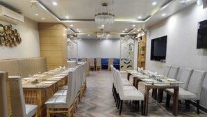 A dining area with long tables and chairs, a patterned floor, and a chandelier. - Hotel Rajvanshi (Gurugram)