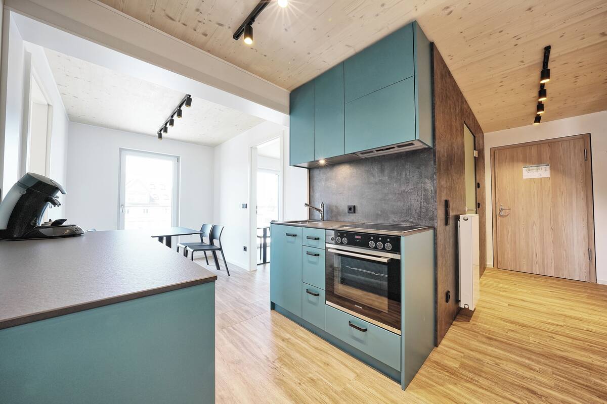 Eine moderne Küche mit türkisblau-grünen Schränken, einem eingebauten Ofen und einer Holz Arbeitsplatte.