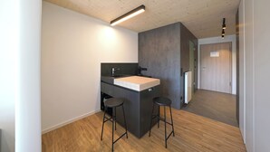 A modern kitchen with a wooden ceiling, a central island with stools, and a built-in sink. - Timber One Boardinghouse Dorfen (Dorfen)