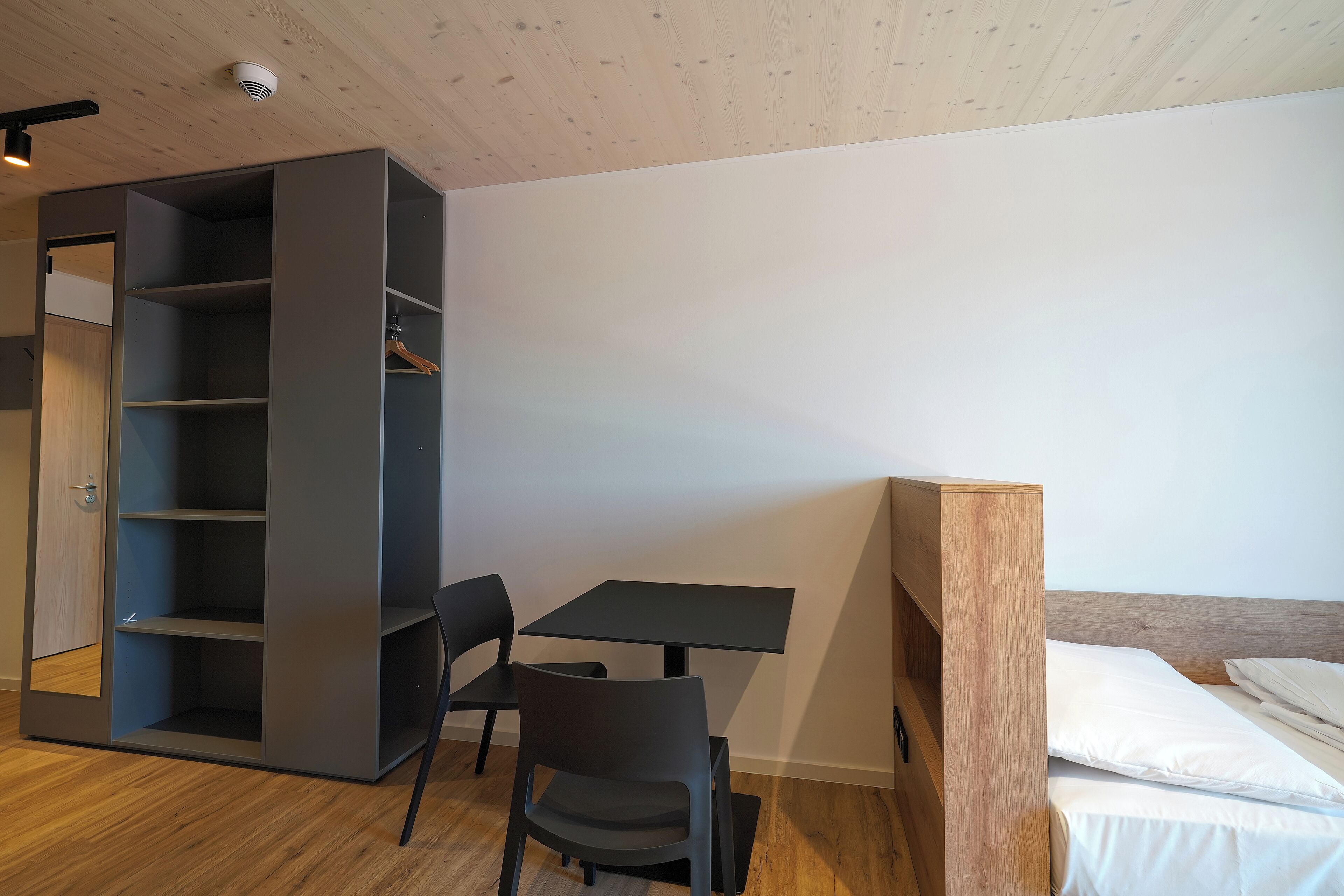 A compact room with a bed, a desk, and a built-in wardrobe.