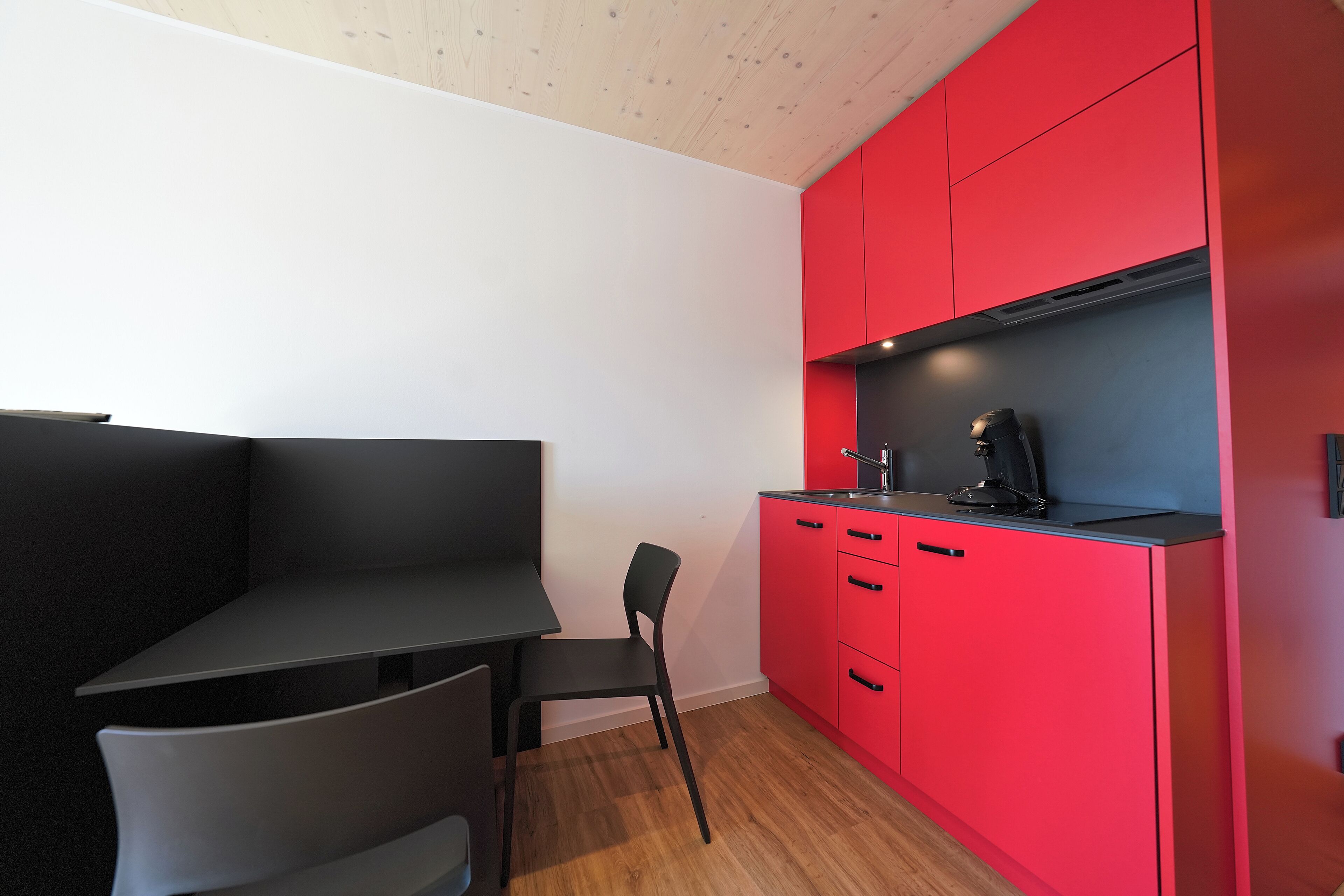 Une cuisine moderne avec des meubles rouges, un plan de travail noir et une chaise noire.