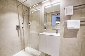 Een moderne badkamer met een douchecabine van glas, een witte wastafel en een spiegel.