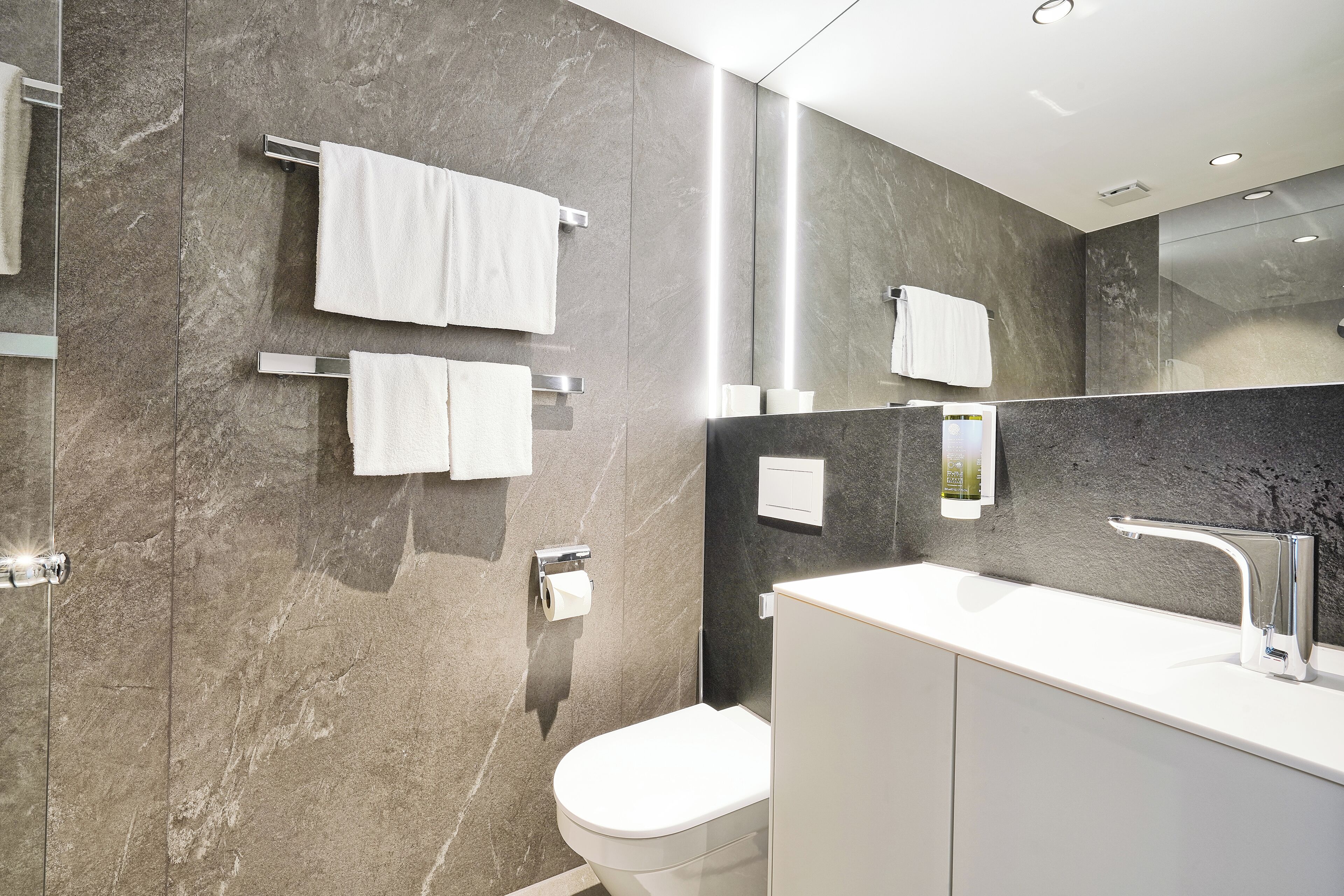 A modern bathroom with a marble wall, a white sink, and a toilet.