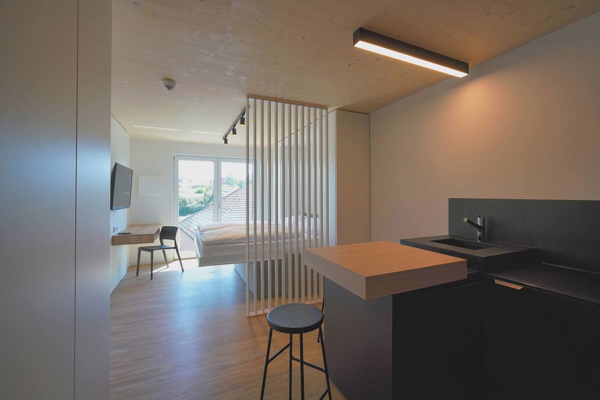 Eine moderne Küche mit einer Holzausziehtafel, einem schwarzen Hocker und Blick ins Freie durch eine Schiebetür.