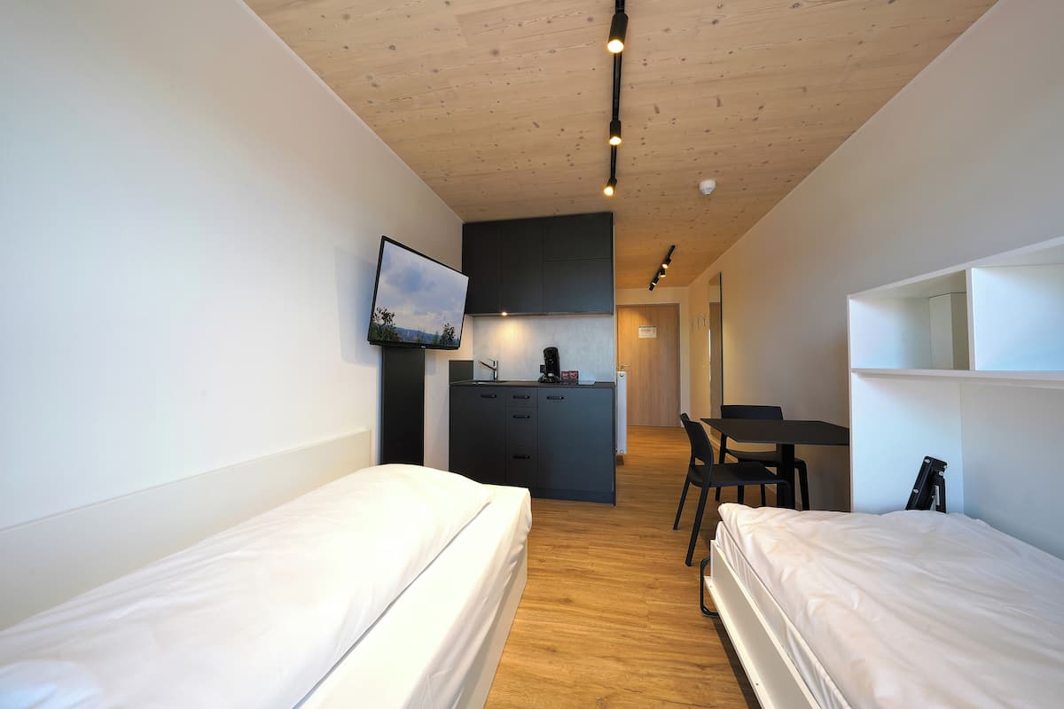 Ein modernes Hotelzimmer mit zwei Einzelbetten, einer Küchenzeile, einem Essbereich und einem an der Wand montierten Fernseher.
