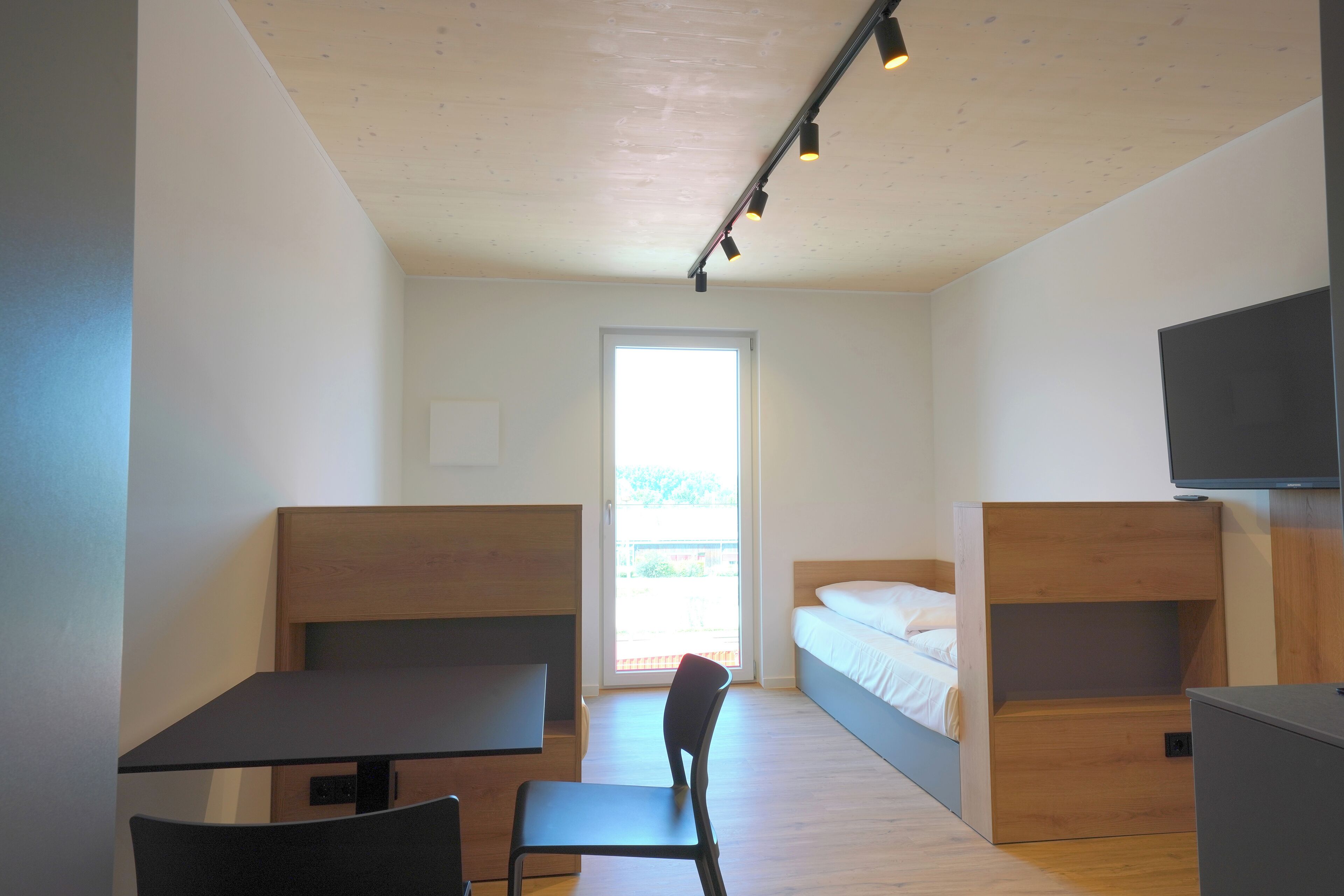 A modern room with a desk, chair, bunk beds, and a TV.