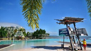 Una piscina cristallina con una postazione di salvataggio, palme e un cartello per Cairns Esplanade.