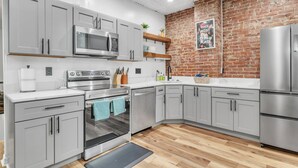A modern kitchen with grey cabinets, stainless steel appliances, and a brick wall accent. - The Smith Victorian 2BR Brownstone Apartment (Springfield)