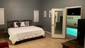 A bedroom with a bed, a wooden nightstand, a TV, and a door leading to a pool area. - As new Santa Fe home, over 2000sf, 4 bedrooms, 2 bathrooms, Pool, Spa. (La Quinta)