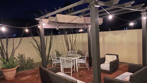 An outdoor patio with a pergola, string lights, a round table with chairs, and wicker furniture. - As new Santa Fe home, over 2000sf, 4 bedrooms, 2 bathrooms, Pool, Spa. (La Quinta)