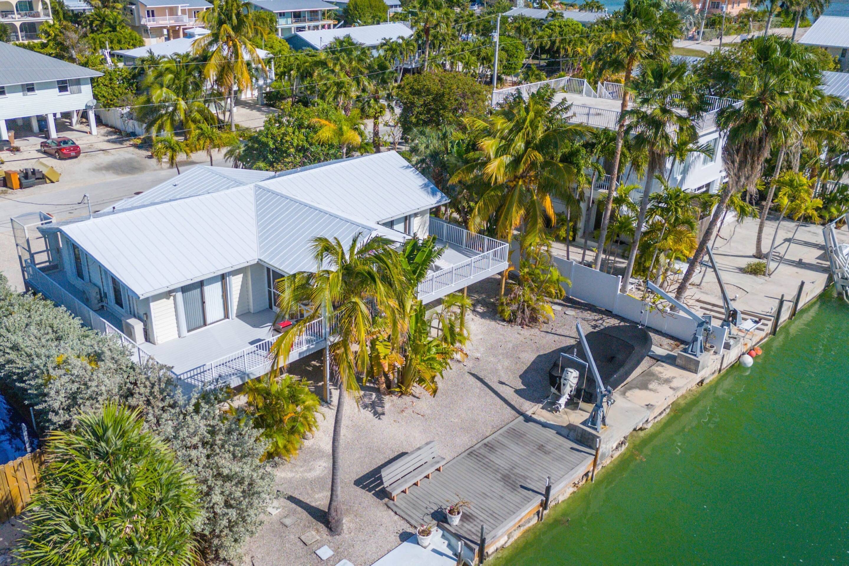 An aerial view of a coastal property with a large building featuring a blue roof, surrounded by palm trees and a dock.
