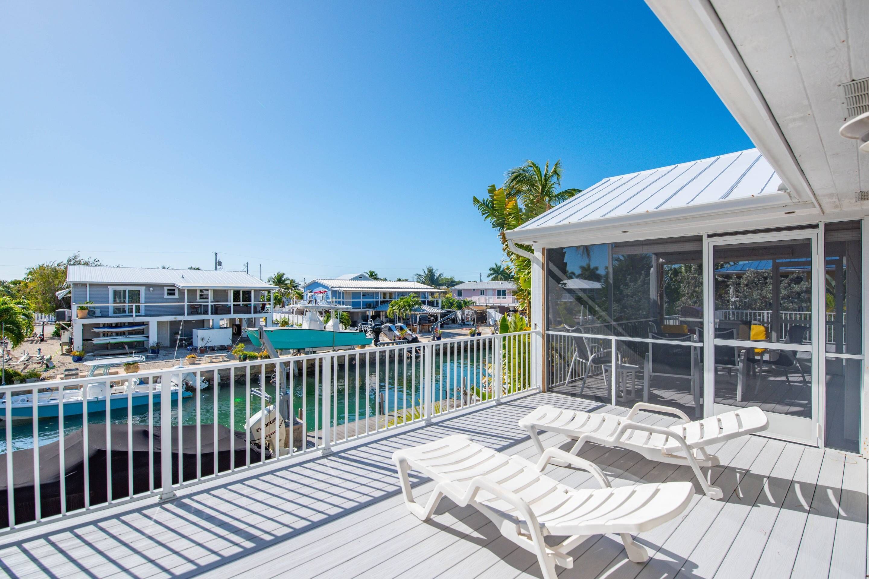 A balcony with white lounge chairs, a pool, and a view of other buildings.