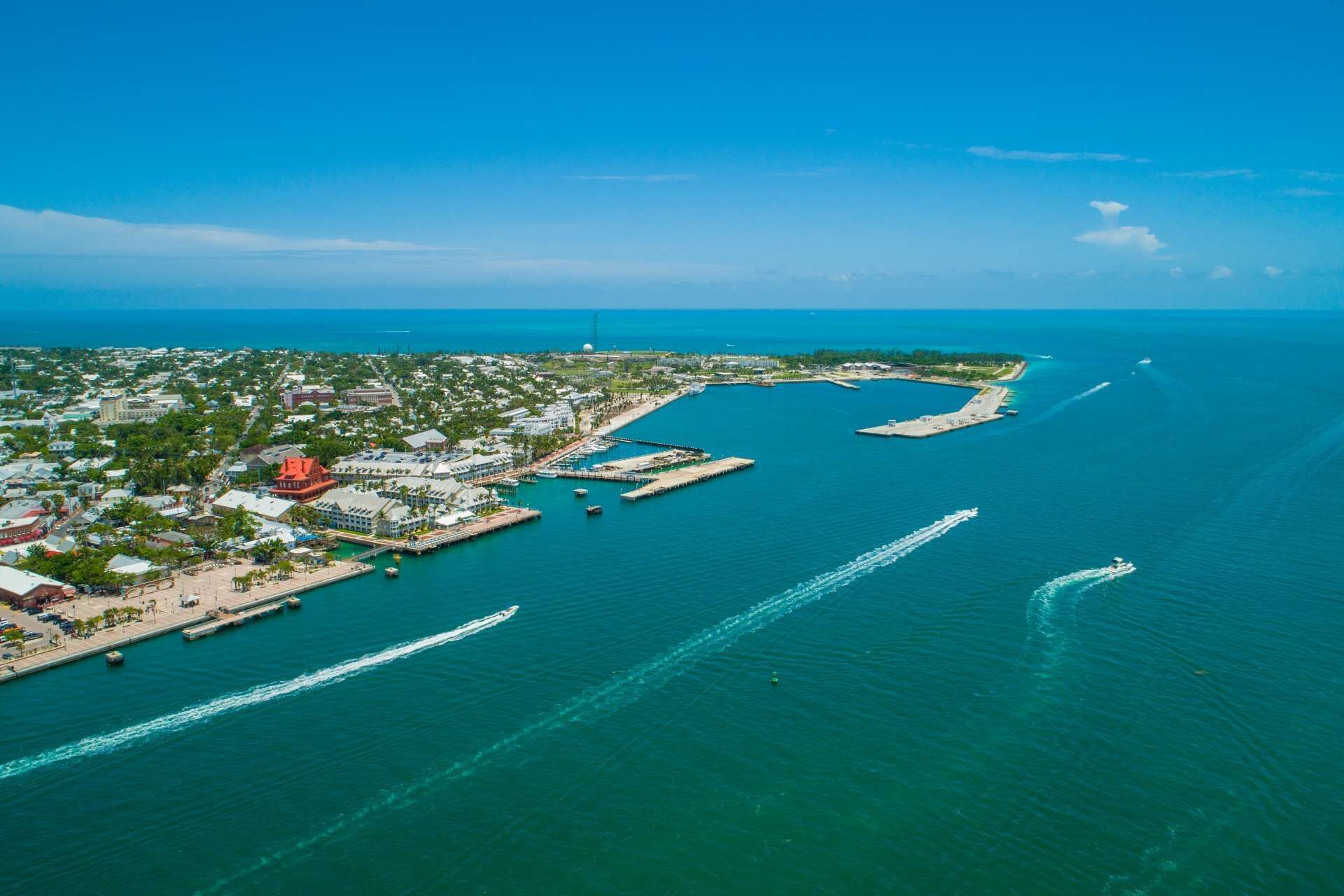An aerial view of a coastal town with a marina, boats, and a clear blue sky.