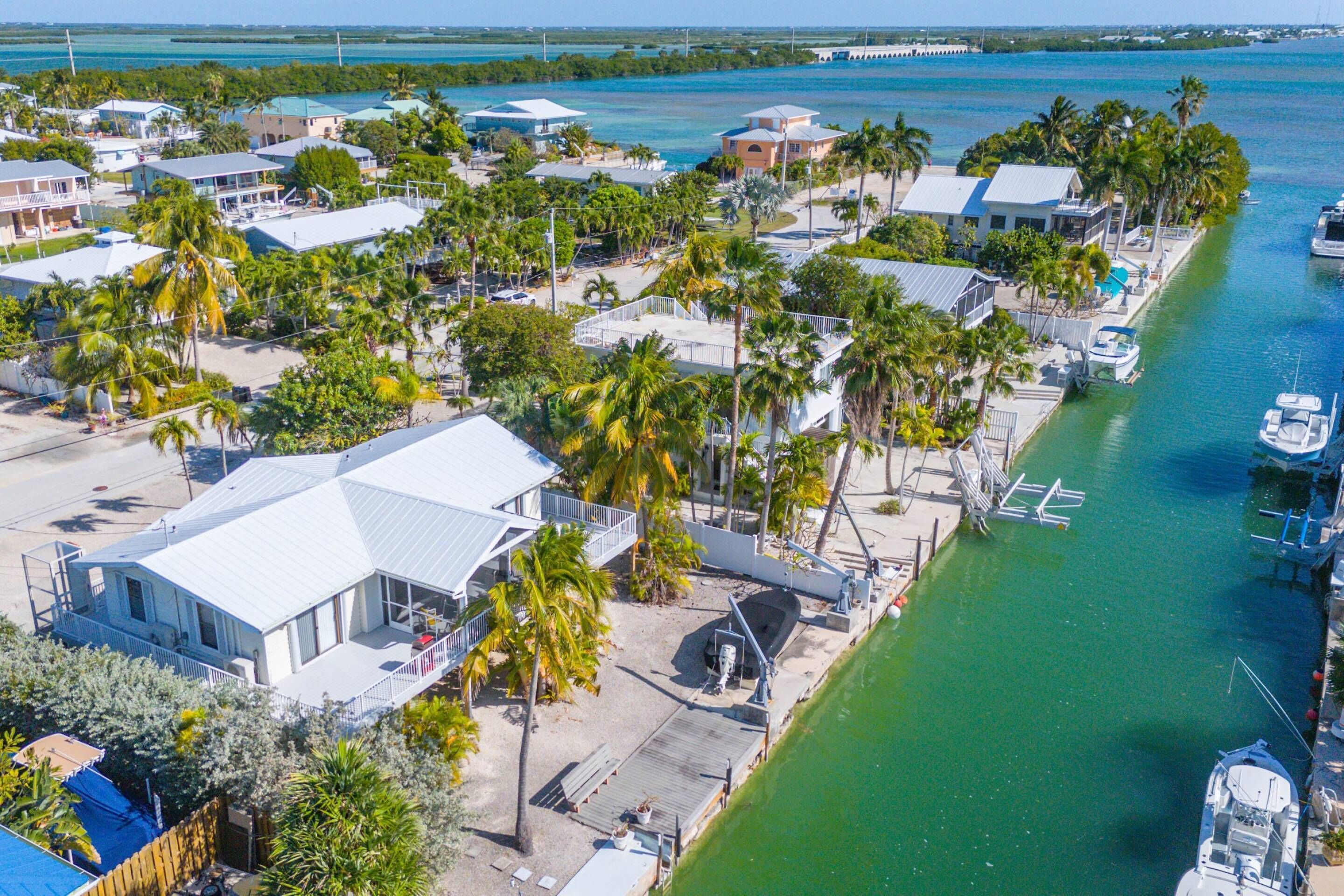 An aerial view of a coastal residential area with houses, a marina, and a clear view of the ocean.