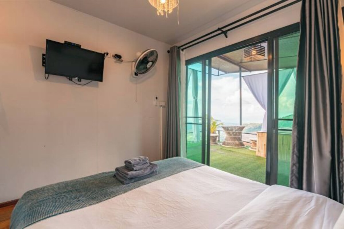 A bedroom with a bed, a television mounted on the wall, and a sliding glass door leading to an outdoor area.