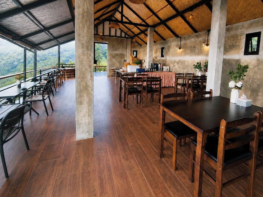 A spacious dining area with high ceilings, wooden flooring, and large windows offering a view of the surrounding landscape.