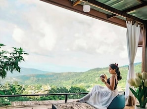 A person sitting on a balcony with a view of a green landscape. - NJ Homestay (Mae Rim)