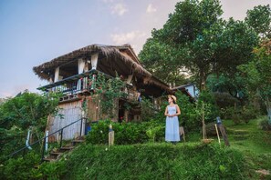Ein rustikales Holzhaus mit einem Reetdach, einem Balkon mit roten Blumen und üppiger, umgebender Bepflanzung.