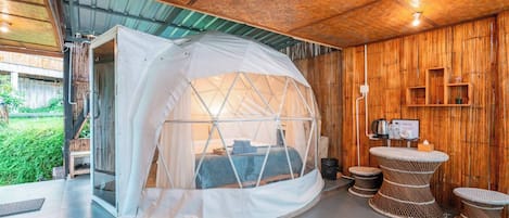 A cozy, enclosed sleeping area with a bed, a small table, and a chair, surrounded by wooden walls and a glass door.