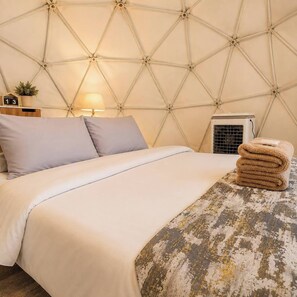 A bed with a geometric patterned headboard, a bedside lamp, a small plant, and a folded towel on the bed. - NJ Homestay (Mae Rim)