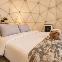 Una cama con cabecera de estampado geométrico, una lámpara de noche, una planta pequeña y una toalla doblada sobre la cama.