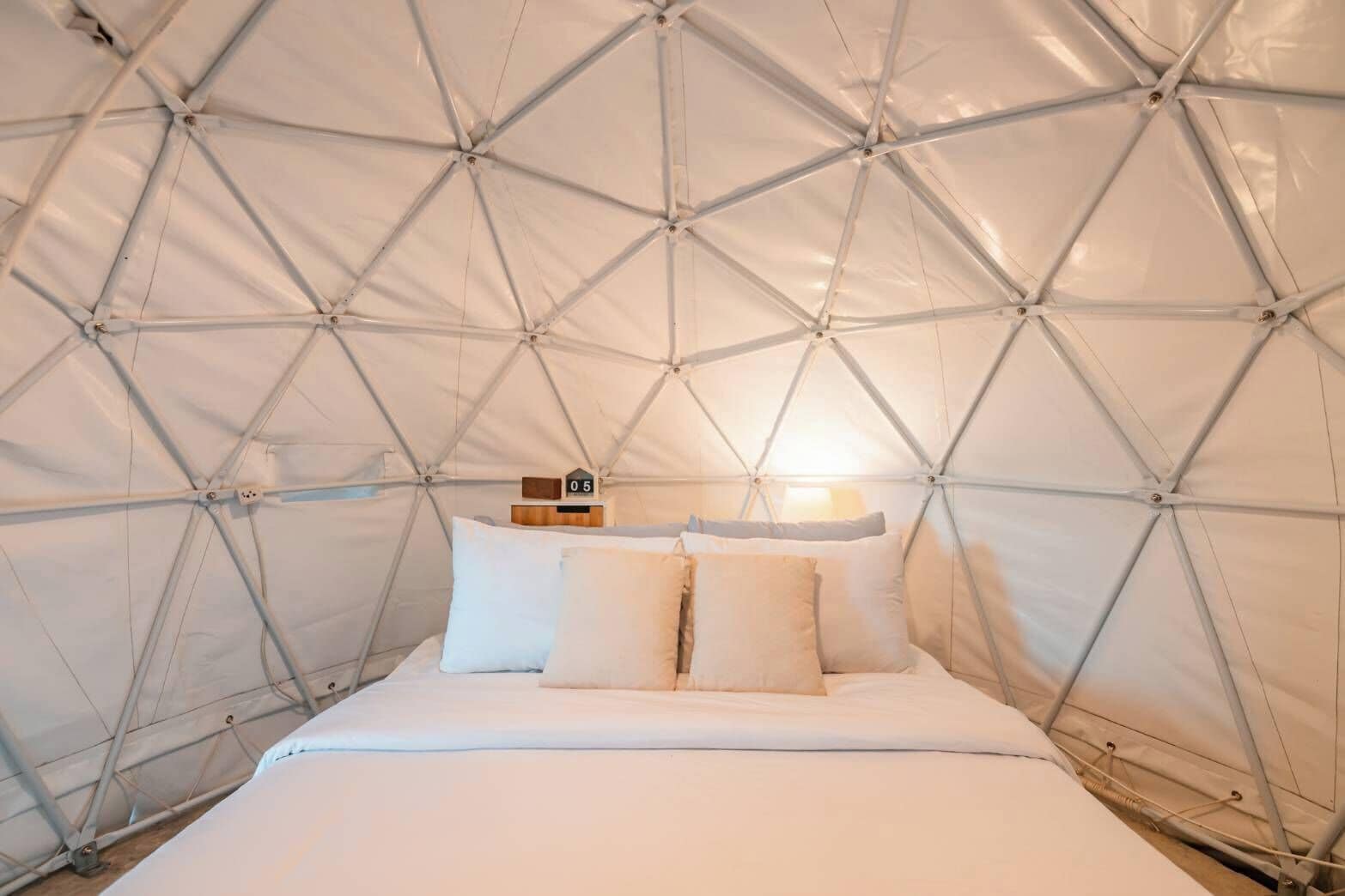 A tent-style room with a bed, pillows, a clock, and a lamp.