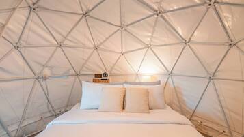 A tent-style room with a bed, pillows, a clock, and a lamp.