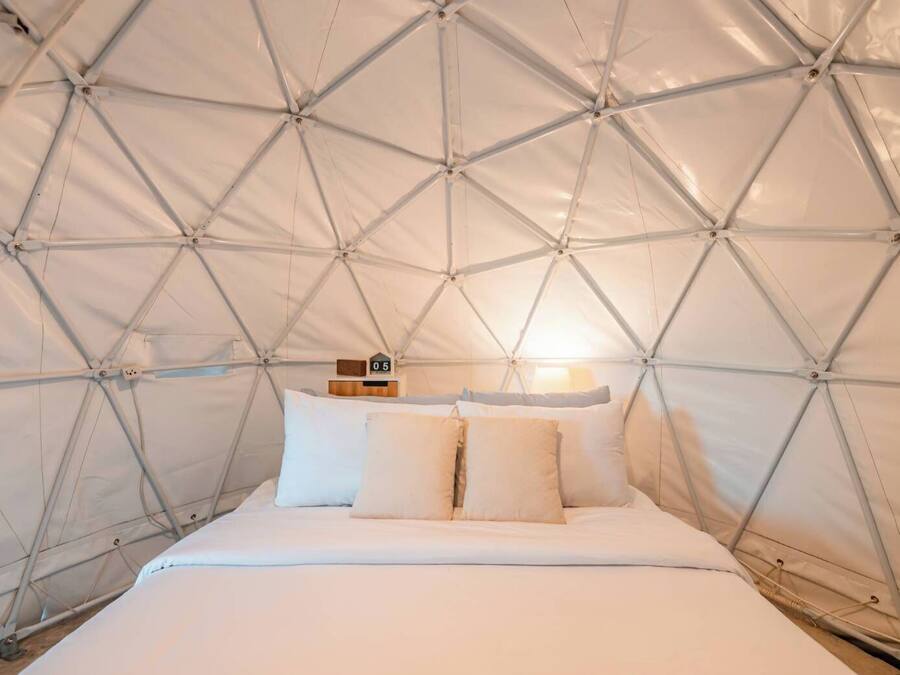 A tent-style room with a bed, pillows, a clock, and a lamp.