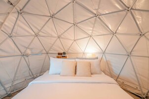 Una habitación tipo tienda de campaña con una cama, almohadas, un reloj y una lámpara.