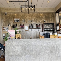 Zona de bar con mostrador de hormigón, botellas de vino, copas y un letrero que dice 'Home'.