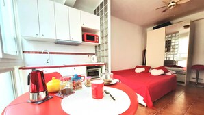 Une chambre d’hôtel compacte, dotée d’une kitchenette, d’un lit avec une literie rouge et d’une table à manger avec des articles pour le petit-déjeuner.