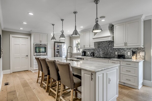 A modern kitchen with white cabinets, a marble island, and pendant lighting.