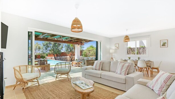 A modern living room with a sofa, chairs, a coffee table, and a dining area. There is a large window providing a view of the outdoors. - Villa Pepponi MENORCA modern, private pool, AC (Sant Lluís)
