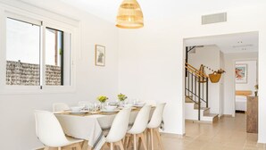 A dining area with a white table set for four, white chairs, a hanging light fixture, and a staircase leading to another room. - Villa Pepponi MENORCA modern, private pool, AC (Sant Lluís)